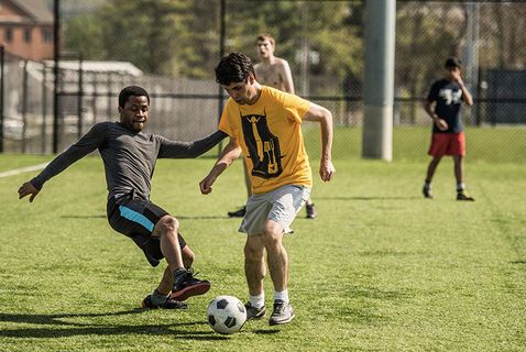 two students playing soccer outside