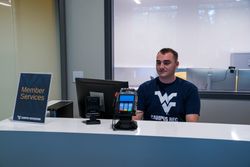WVU Campus Rec worker at the front desk of Downtown Fitness center, computer, point of sale, and "Member Services" sign